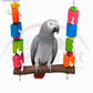 A grey parrot perched on a wooden hanging toy with colorful stacked blocks in orange, yellow, green, blue, and pink, shown against a white background with a Petsmart logo.Bird Blocks natural wooden swing 30 by 31cm with colourful blocks rope and hanging chains