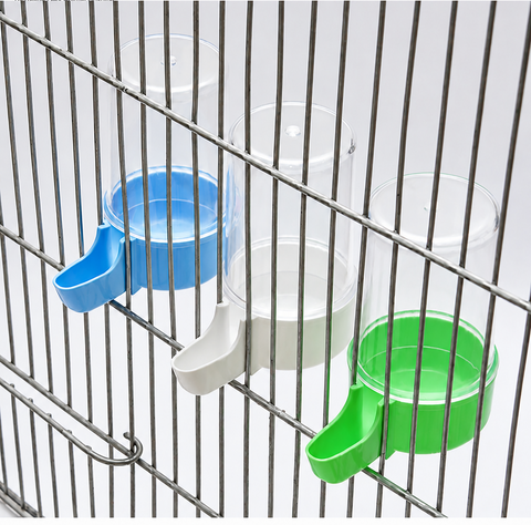 Three clear plastic pet water bottles with blue, white, and green dispensers mounted on a metal wire cage. The Petsmart logo is visible in the top left corner, and a red contact banner is at the bottom.